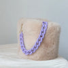 A light beige faux fur bag with a purple chain strap resting on white fabric.