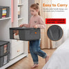 A young girl is carrying a gray foldable storage bag with a double-sided handle in a brightly lit room.