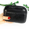 A black PU leather mini wallet with a zipper and keychain is held in a hand against a white background.