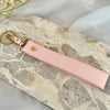 A pink leather wristlet keychain is displayed on a light stone surface.