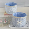 Cesta de almacenamiento acolchada de algodón a cuadros blancos y azules con un lazo de cinta blanca sobre una bandeja gris.