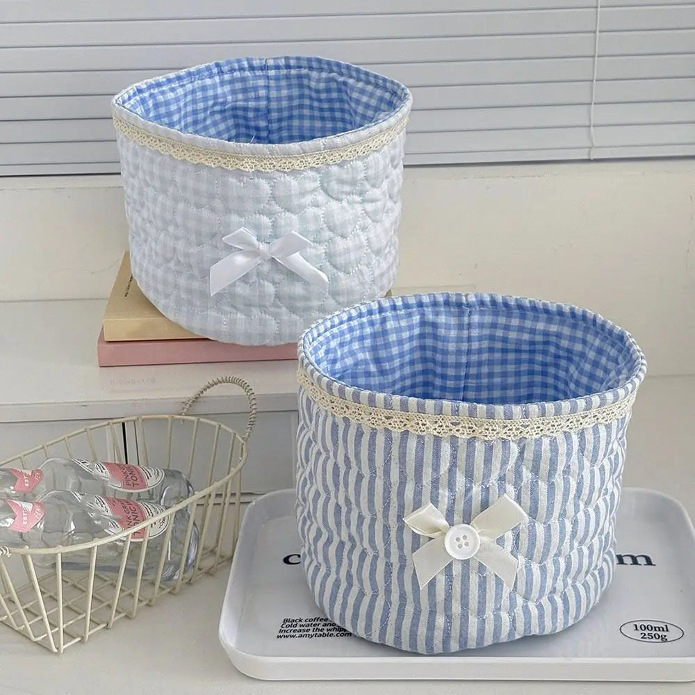 Cesta de almacenamiento acolchada de algodón a cuadros blancos y azules con un lazo de cinta blanca sobre una bandeja gris.