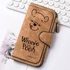 A brown leather zippered coin purse featuring a Winnie the Pooh face design resting on a white background next to a keyboard.
