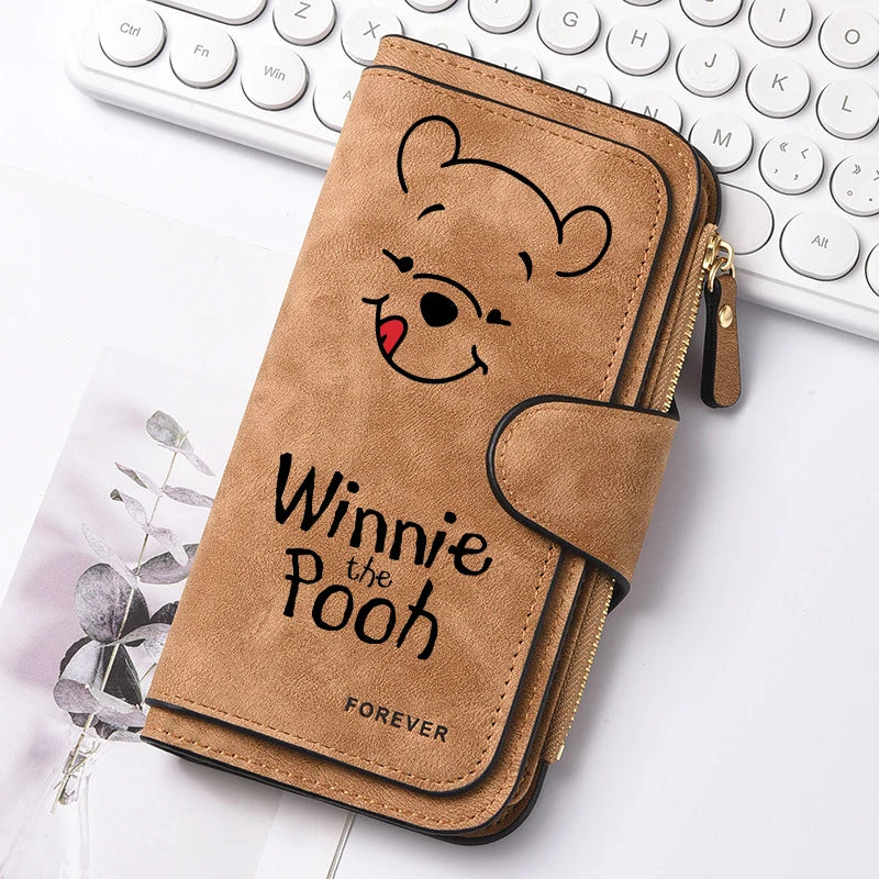 A brown leather zippered coin purse featuring a Winnie the Pooh face design resting on a white background next to a keyboard.