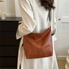 A close-up of a brown leather shoulder bag with a decorative strap carried by a person wearing a white coat.