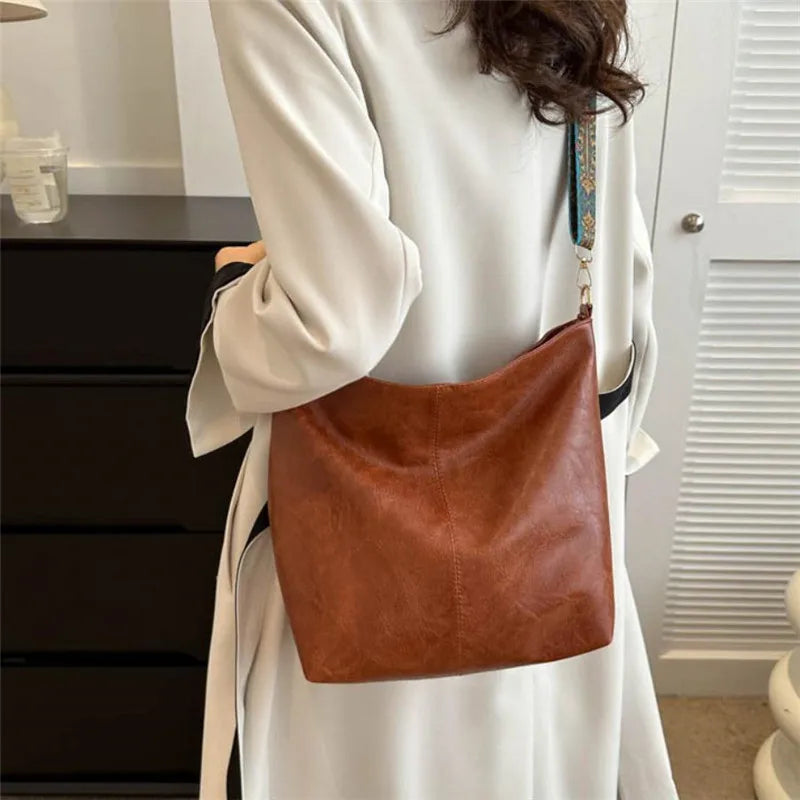 A close-up of a brown leather shoulder bag with a decorative strap carried by a person wearing a white coat.
