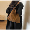 A woman is holding a tan suede slouchy shoulder bag against a black coat.