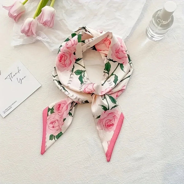 Rosa und grün gemusterter Seidenschal mit Schleife auf weißem Stoff neben einem Parfümflakon.