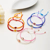 A collection of colorful beaded friendship bracelets in various colors like orange, red, purple, and pink laid out on a white