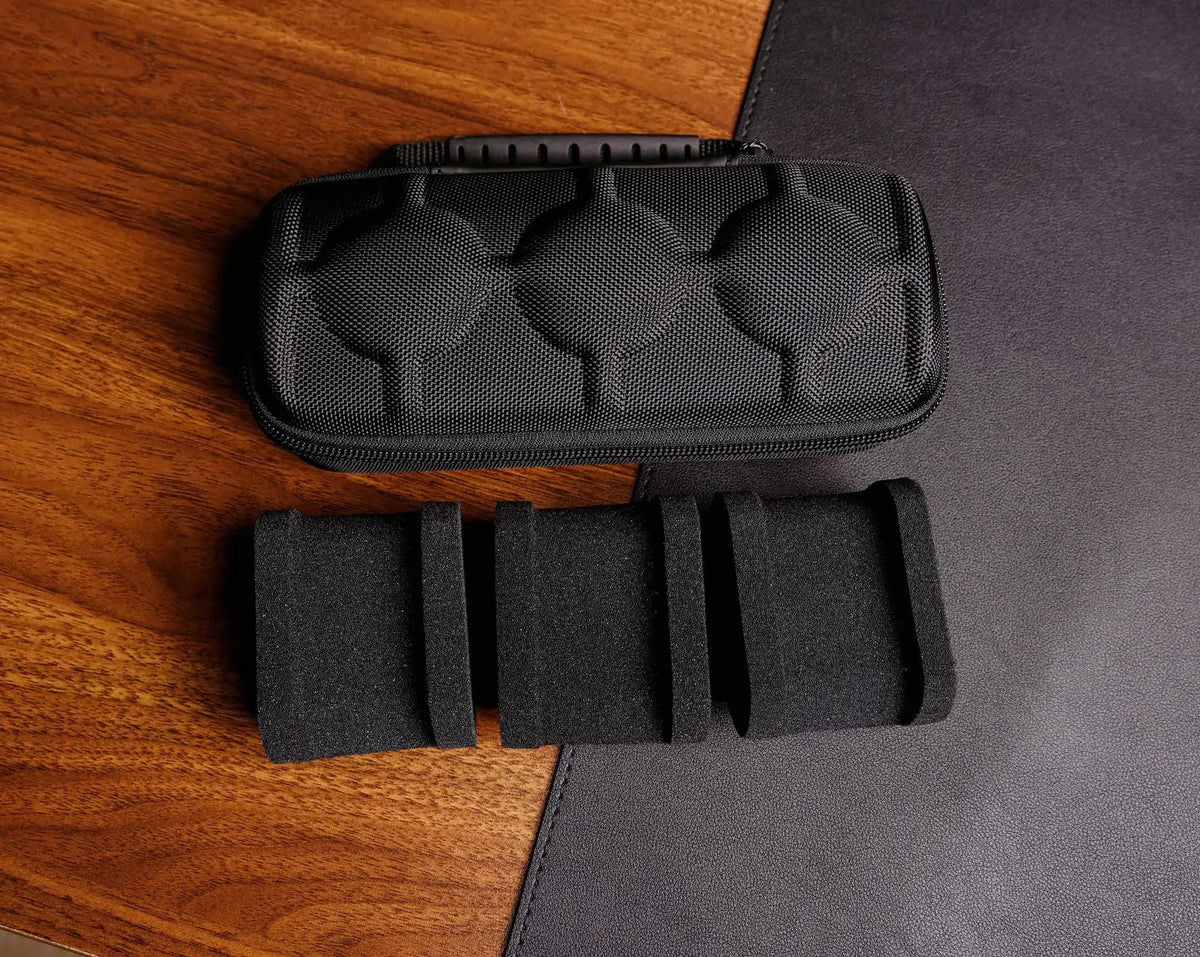 Black multi-slot travel watch organizer case with soft lining placed on a dark gray surface.