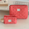 A red and white plaid cosmetic storage bag is shown lying on a white surface.