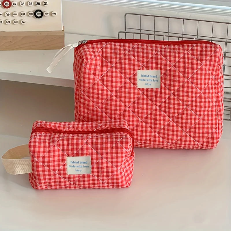 A red and white plaid cosmetic storage bag is shown lying on a white surface.