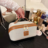 A beige travel toiletry bag with a brown leather trim and gold hardware is shown on a dark surface.