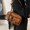 A brown leather vintage letter print crossbody bag carried by a person wearing a black coat.