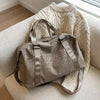 A taupe leopard print duffle bag resting on a light-colored sofa next to a cream knit sweater.