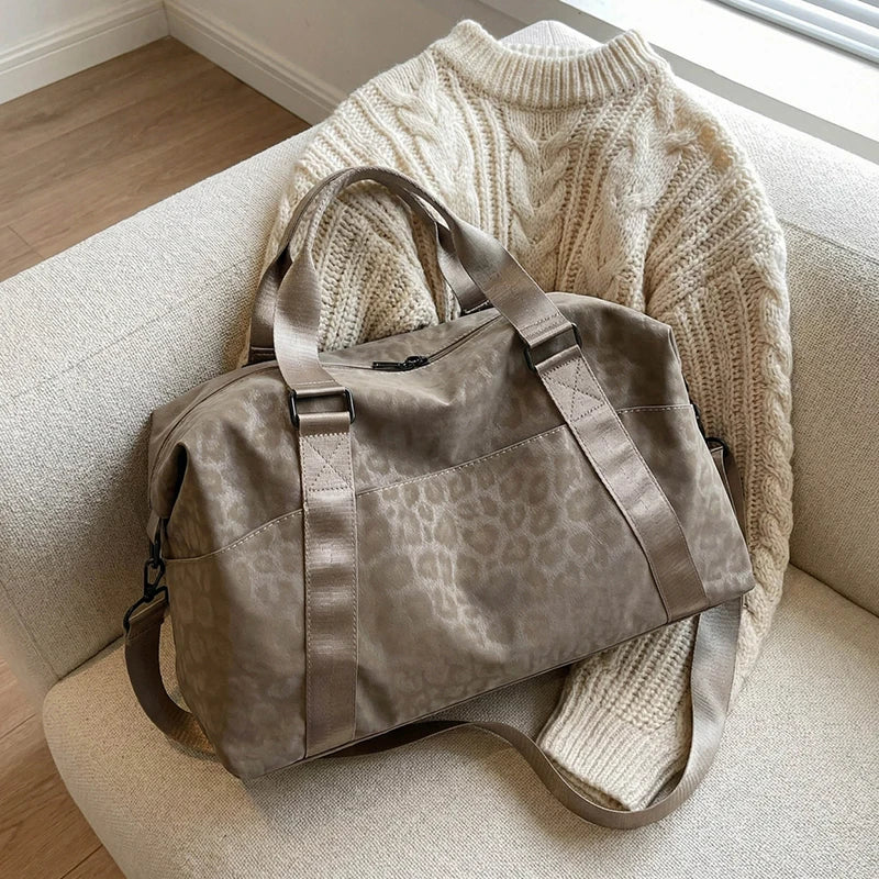 A taupe leopard print duffle bag resting on a light-colored sofa next to a cream knit sweater.