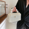 A close-up of a white pearl beaded clutch bag with a strap held by a person against a light background.
