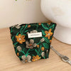 A dark green cosmetic pouch featuring a floral pattern of yellow and gray flowers resting on a wooden surface.