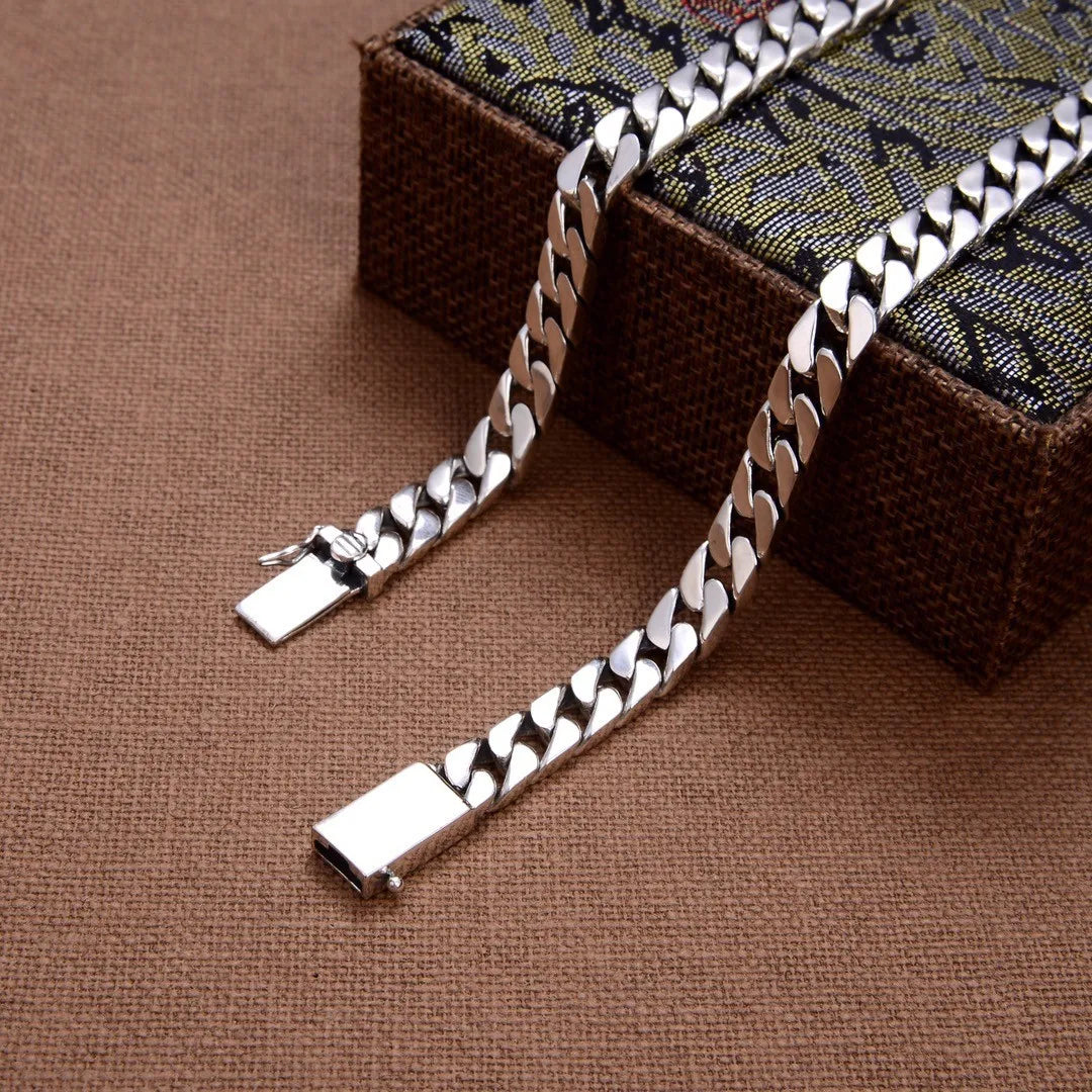 Sterling silver punk charm bracelet with a padlock clasp resting on a dark fabric box.