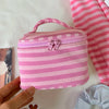 A pink striped makeup bag with a flip-top mirror is held by a hand on a white surface.