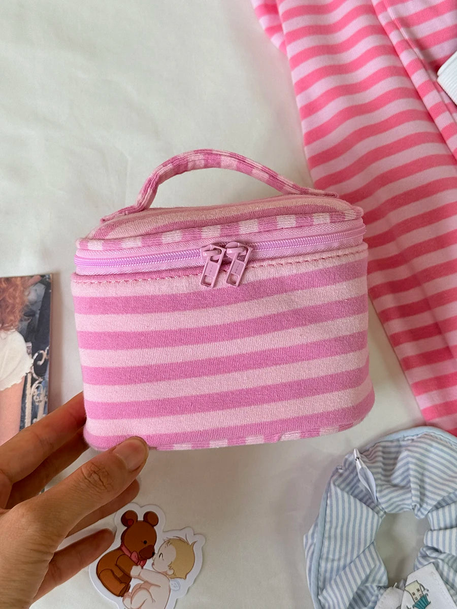 A pink striped makeup bag with a flip-top mirror is held by a hand on a white surface.