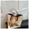 A beige canvas shoulder tote bag with brown leather accents resting on a black leather couch.