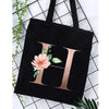 Black canvas tote bag featuring a large gold letter H with floral accents