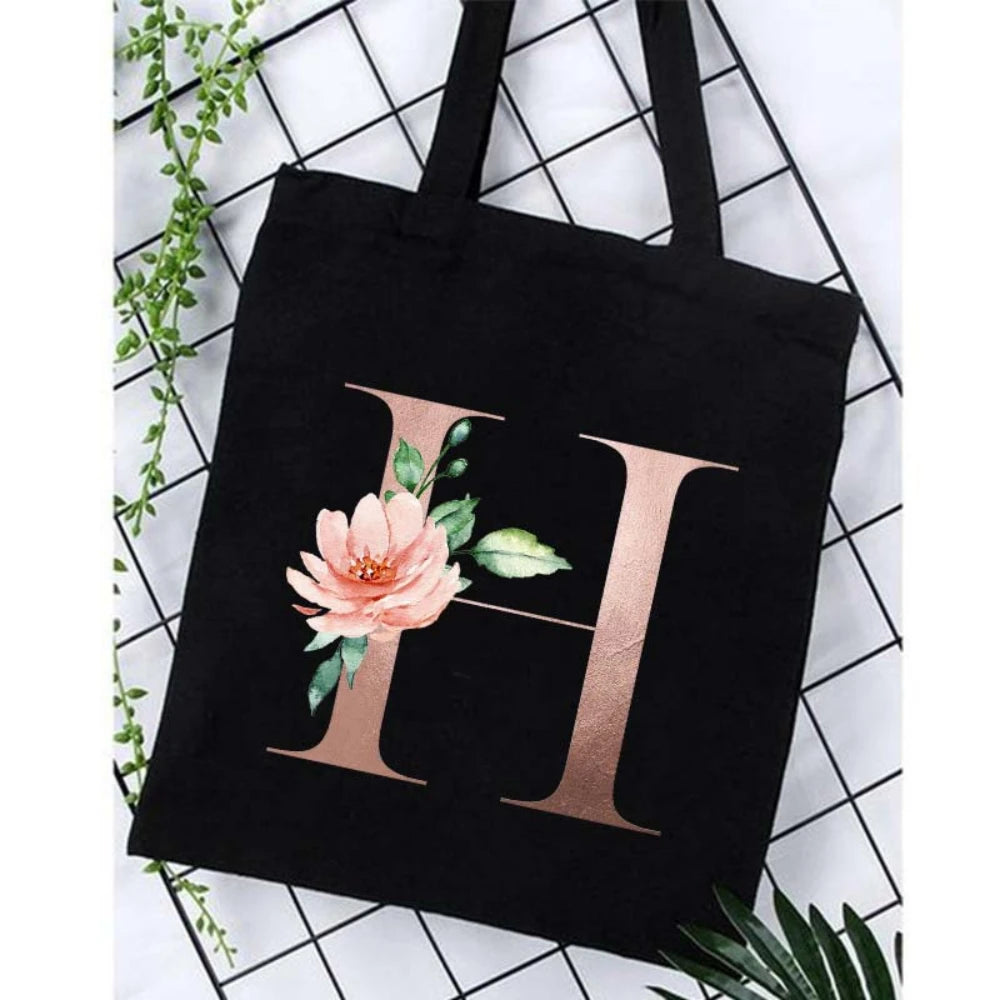 Black canvas tote bag featuring a large gold letter H with floral accents