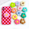 A pink checkered phone case is displayed next to several colorful, flower-shaped silicone grips.