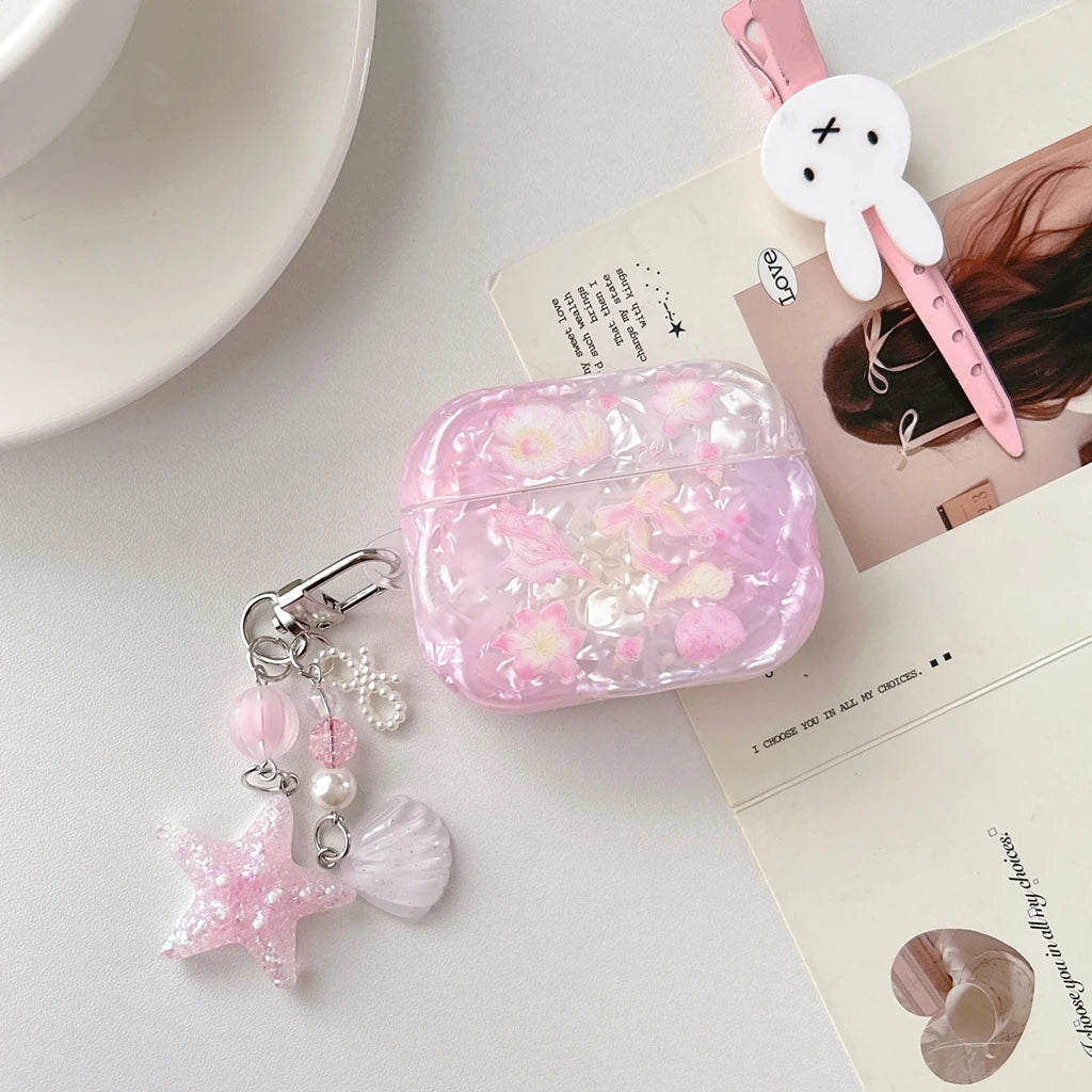 Étui d'écouteurs AirPods avec nœud de fleur rose et charms argentés sur une surface blanche.