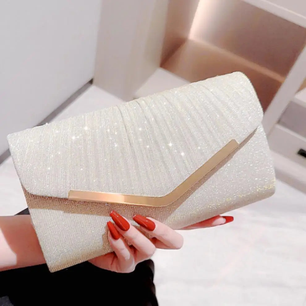 A hand holds a light gold glitter pleated clutch bag with a gold chain against a white background.