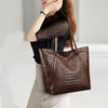 A close-up of a brown crocodile print tote bag carried by a woman.
