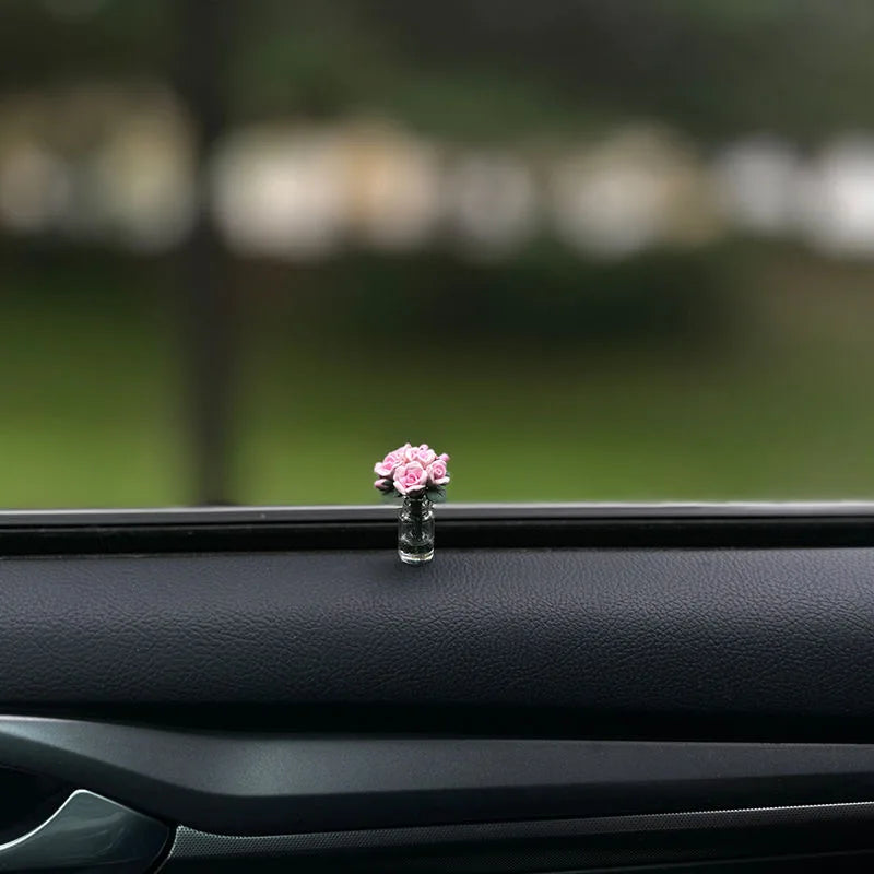 Eine kleine rosa Blumenanordnung in einer Glasvase auf der Innenseite eines Autosfensters.