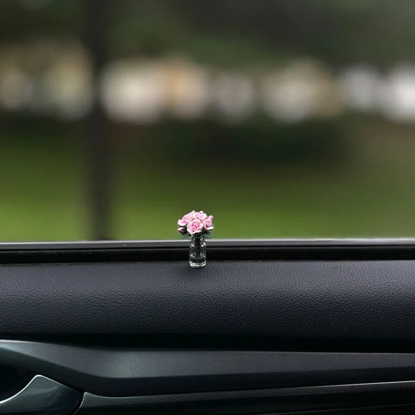 Un petit arrangement floral rose dans un vase en verre placé sur la surface intérieure d'une vitre de voiture.
