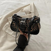 Un sac à main en cuir de fausse peau à imprimé léopard noir, tenu sur un fond beige clair.