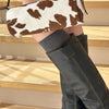 A close-up of a brown and white cow print leather cylinder shoulder bag worn by a person, paired with dark boots.