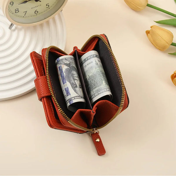 A brown leather compact wallet with a gold zipper, showing a vintage letter print inside.