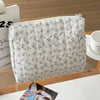 A light blue and white floral patterned quilted cosmetic bag with a zipper, resting on a wooden surface.