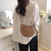 A person is holding a beige handmade rattan straw crossbody bag while wearing a white shirt in a bright room.