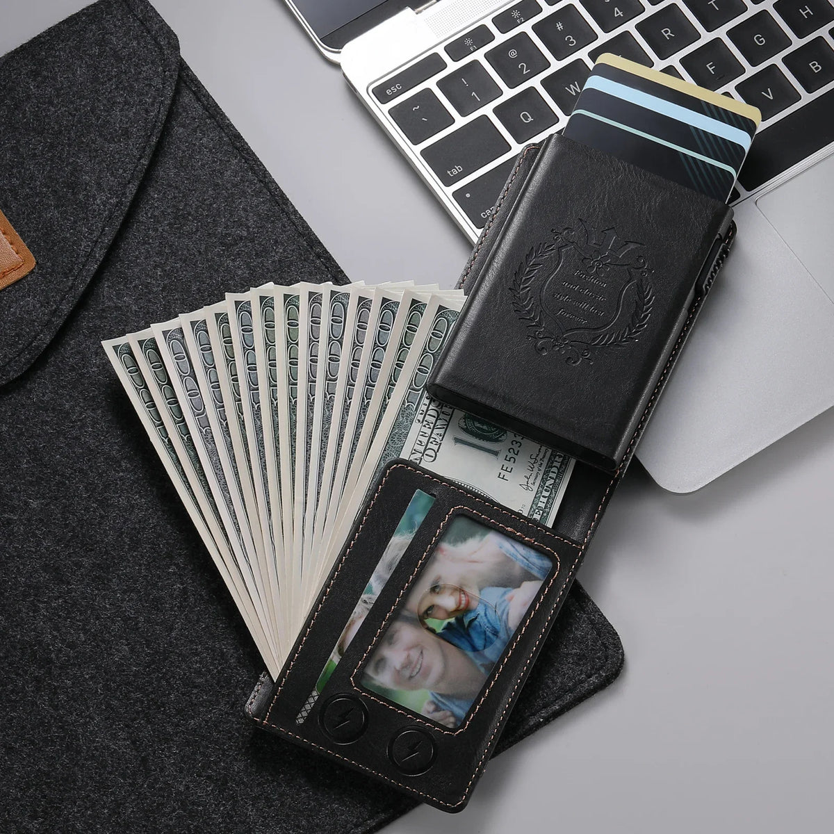 A black anti-RFID blocking PU leather card holder is shown next to a laptop and a stack of US dollar bills.