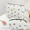 A quilted white makeup bag with black trim and a gold accent is shown on a white surface.