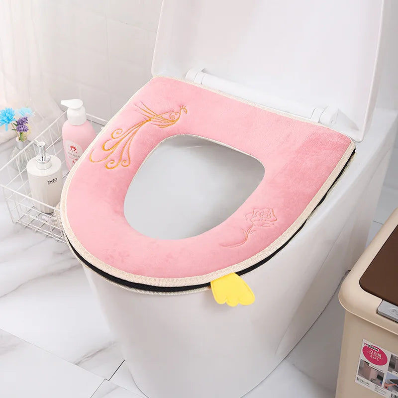 A pink plush waterproof toilet seat cover with a gold floral design is shown inside a white toilet bowl.