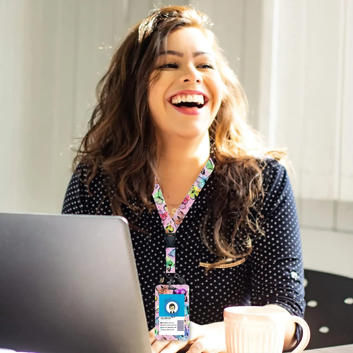 A woman smiling while holding a retractable badge reel with a colorful lanyard and a laptop.