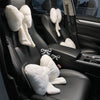 A black car interior showing a seat with a white fluffy bowknot headrest pillow and lumbar support cushion.