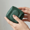 A hand holds a dark green, textured leather coin purse with a snap closure.