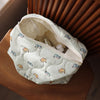 A white quilted cosmetic storage pouch with a light blue and orange cat print is resting on a wooden surface.