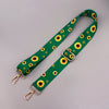 A green strap with a yellow sunflower pattern and metal hardware for an adjustable crossbody bag.