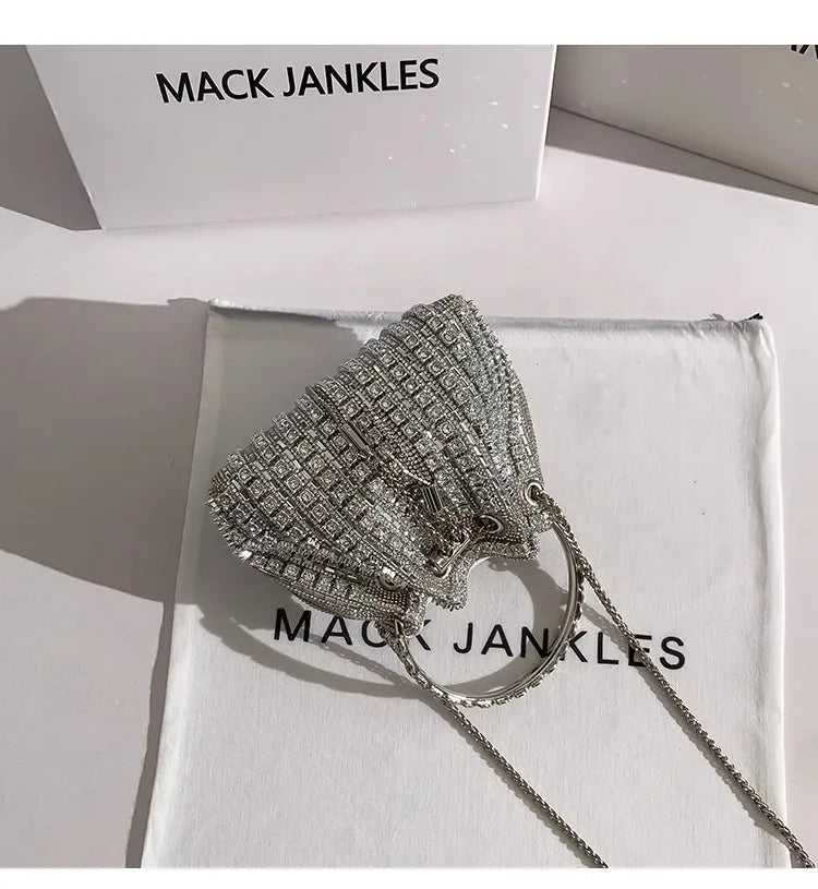 Silver crystal-embellished evening clutch with a delicate chain, displayed on white fabric.