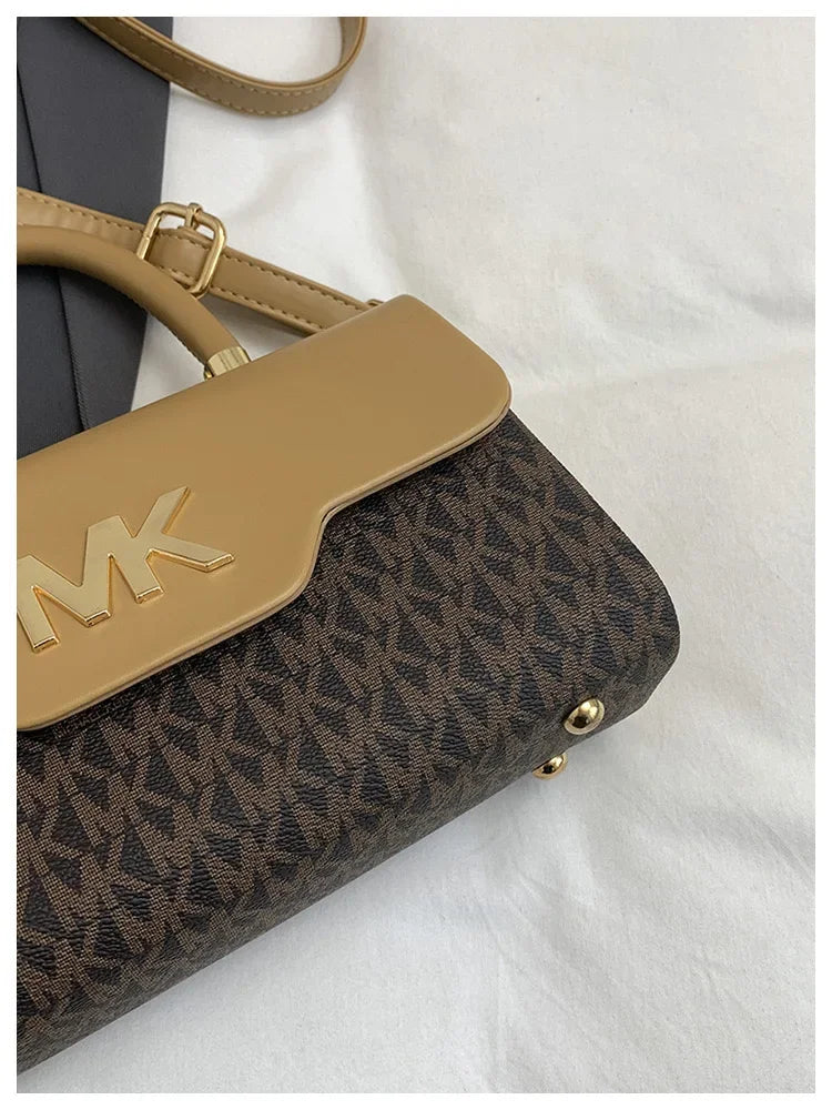 A tan Michael Kors letter square crossbody bag with a brown and black monogram pattern resting on a white surface.
