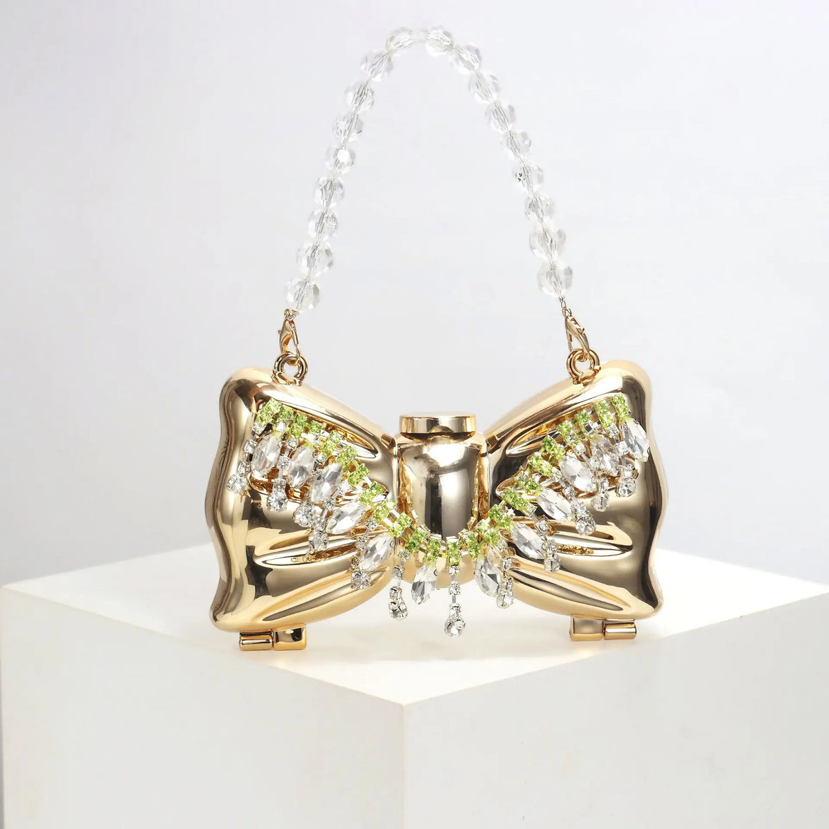 Gold acrylic bow clasp mini handbag with a clear crystal chain strap displayed on a white surface